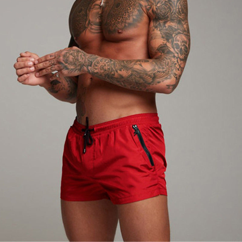 Person wearing red swim shorts with tattoos on arms and chest against a gray background