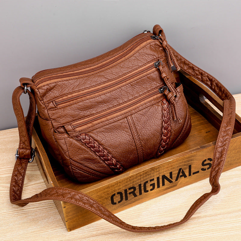 Brown leather handbag with braided details on a wooden box labeled 'ORIGINALS'.