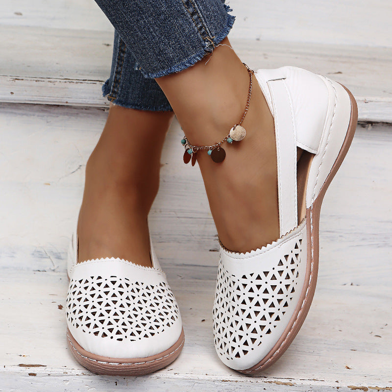 White perforated shoes with brown soles worn with blue jeans on a light wooden floor.