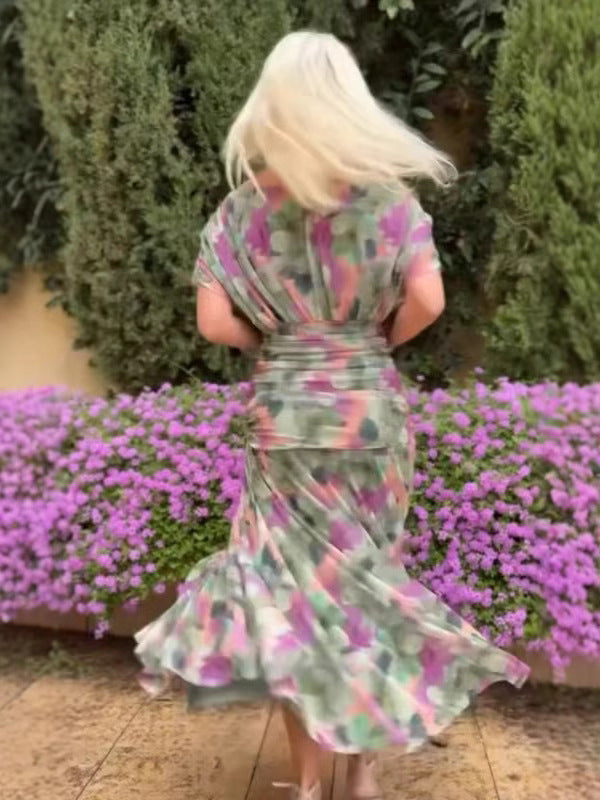 Woman in a floral dress standing in front of pink flowers and green bushes