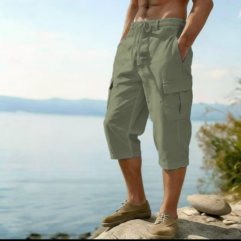 Person wearing green cargo shorts standing by a body of water with mountains in the background.