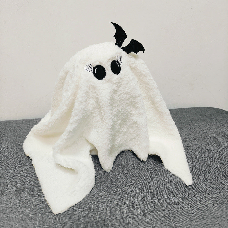 White ghost-shaped plush toy with black eyes and a bow on a gray surface