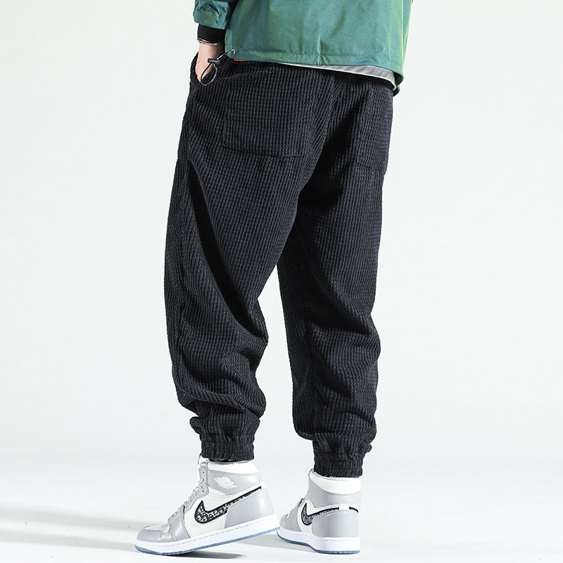 Person wearing black textured pants and white sneakers on a light gray background
