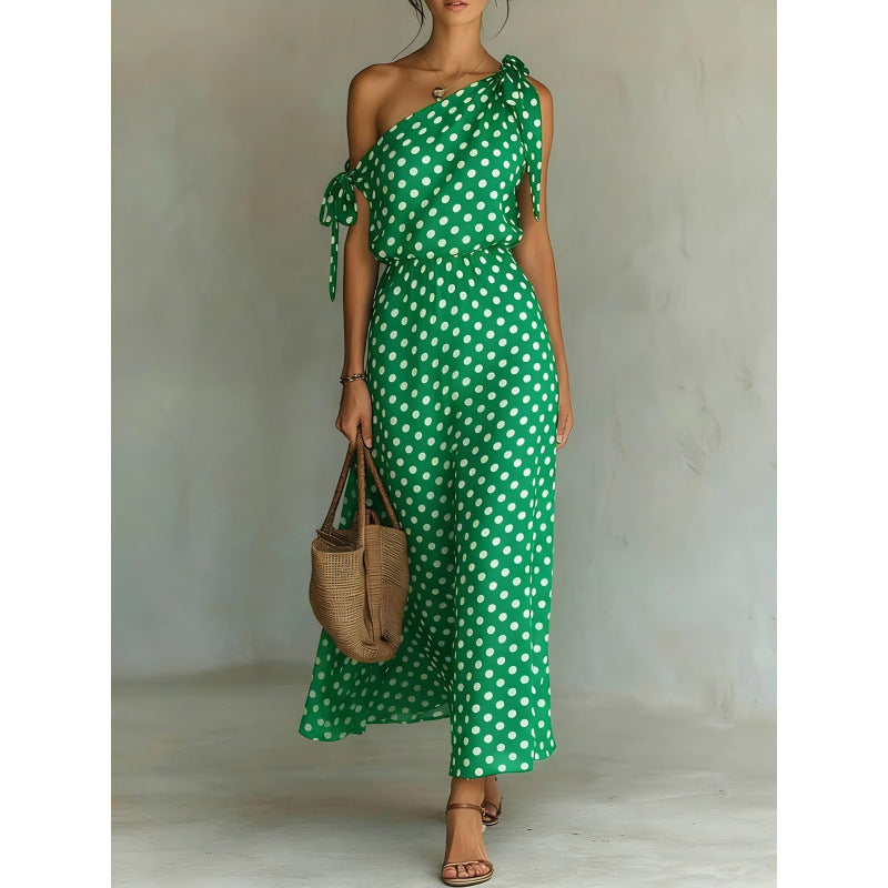Woman wearing a green polka dot jumpsuit holding a woven bag against a neutral background