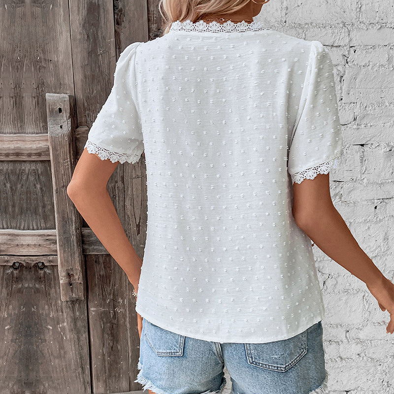 Person wearing a white polka dot blouse with lace trim in front of a wooden door and white wall.