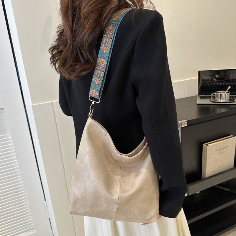 Person wearing a beige handbag with a decorative strap in an indoor setting