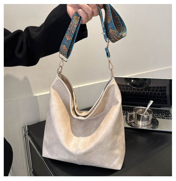 Beige handbag with a patterned strap held by a person in a kitchen.