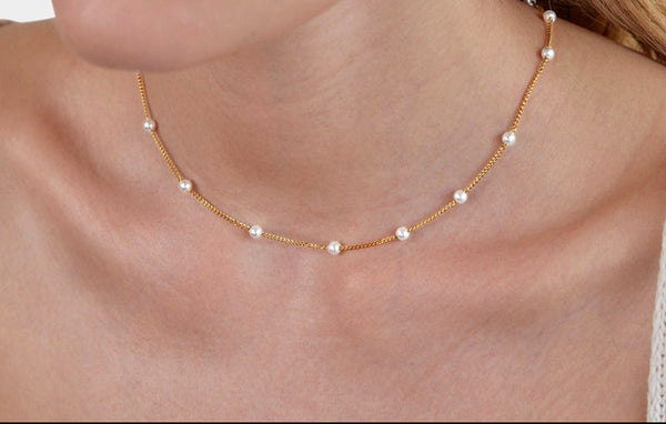 Close-up of a woman wearing a gold necklace with pearls on a plain background