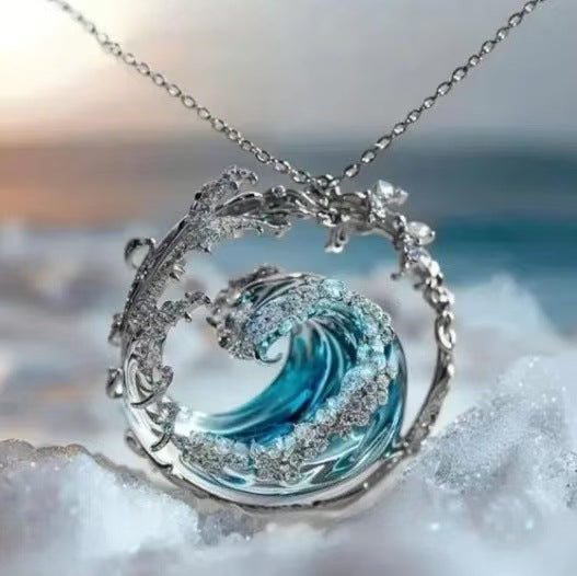 Wave-shaped pendant necklace with blue center and silver frame on a blurred beach background