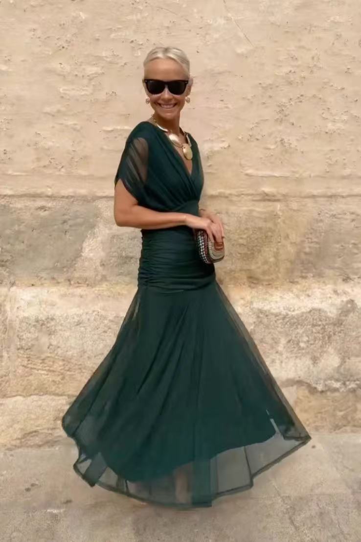 Woman wearing a green dress standing against a stone wall.