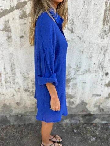 Woman in loose blue shirt dress from ZA-Zola, standing outdoors against a textured wall