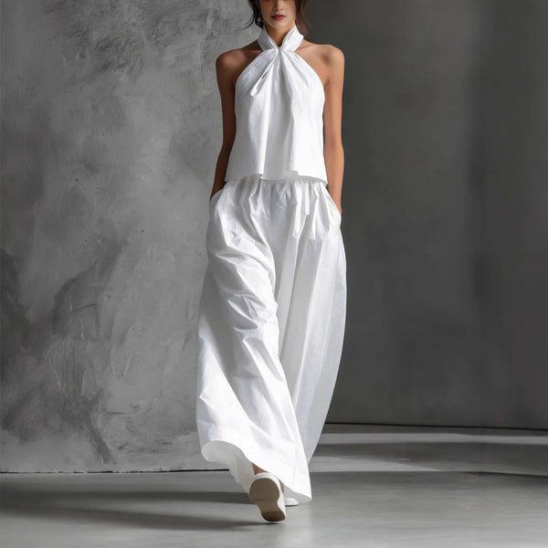 Woman wearing a white halter top and wide-leg pants against a gray background