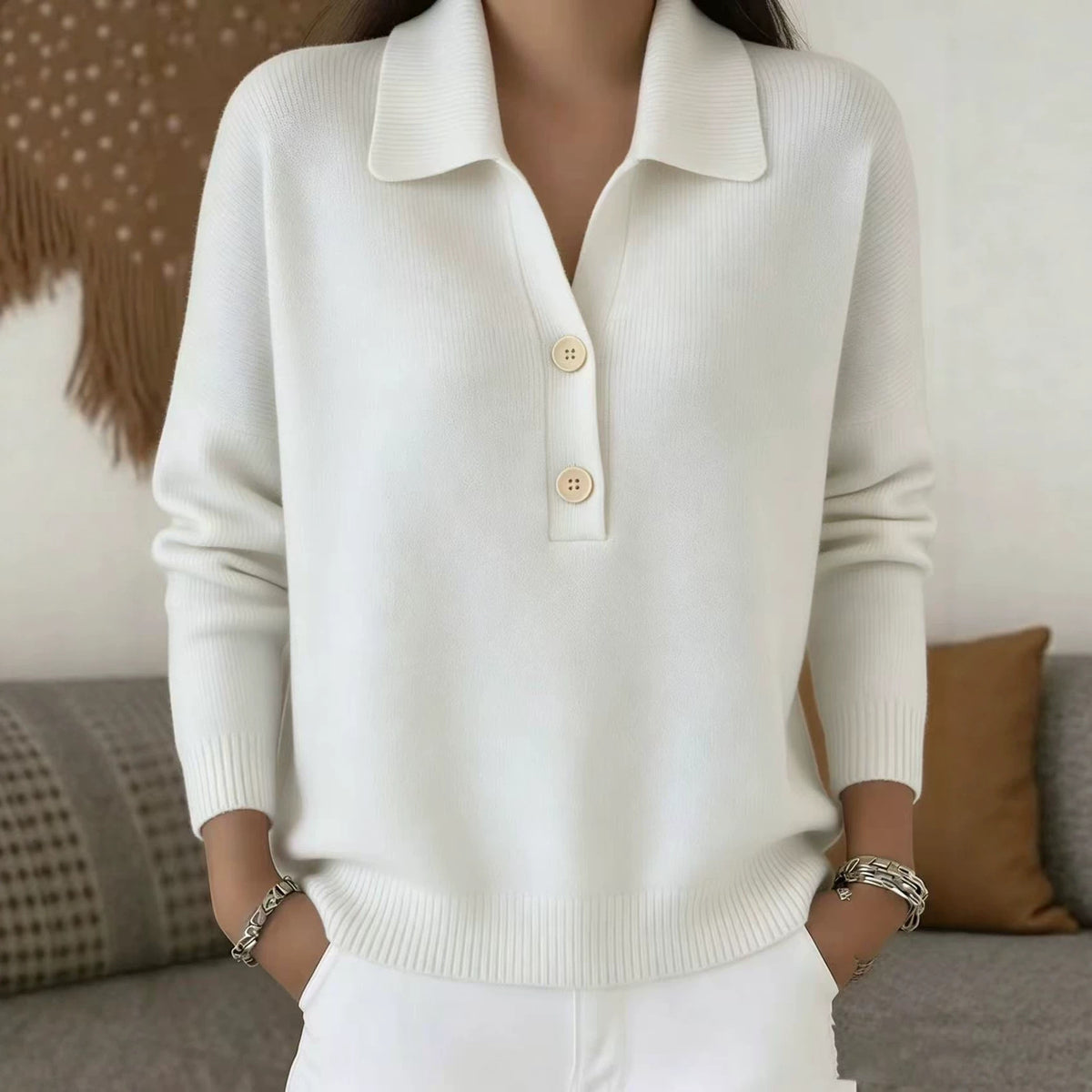 White sweater with button details worn by a person, sitting on a couch.
