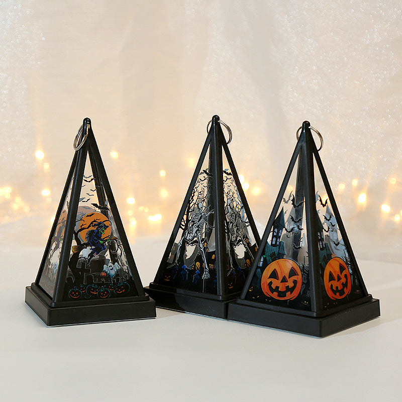 Three black pyramid-shaped Halloween lanterns with hanging loops, decorated with spooky cutout scenes including a witch on a broomstick, bats, haunted trees, and jack-o'-lanterns, displayed on a white surface against a softly lit warm background.