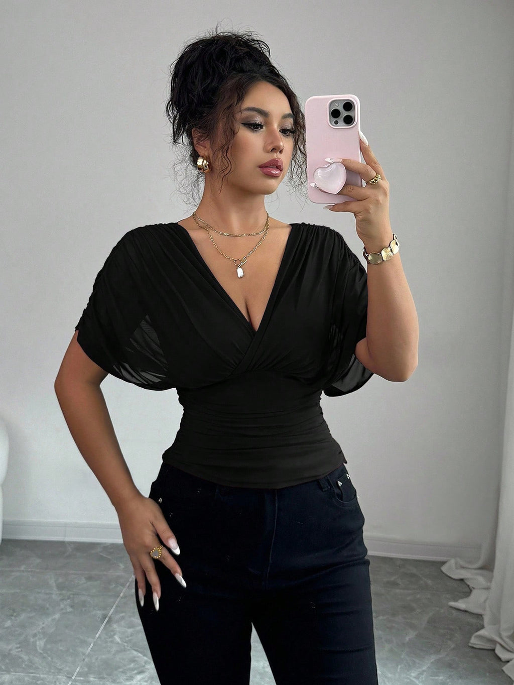 Woman taking a mirror selfie wearing a black top and black pants in a neutral setting.