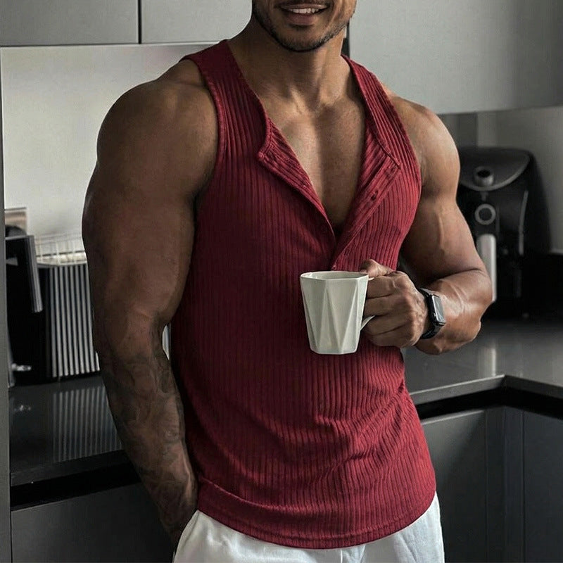 Man in a red tank top holding a white mug in a kitchen.