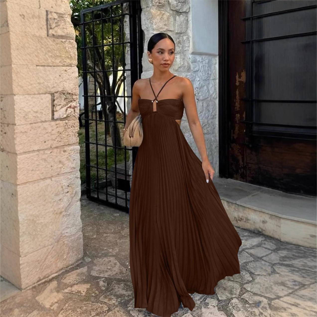 Woman in a brown dress standing outside a building with stone walls.