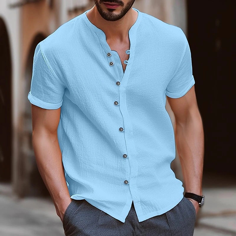 Man wearing a light blue short-sleeve shirt with buttons, standing outdoors.