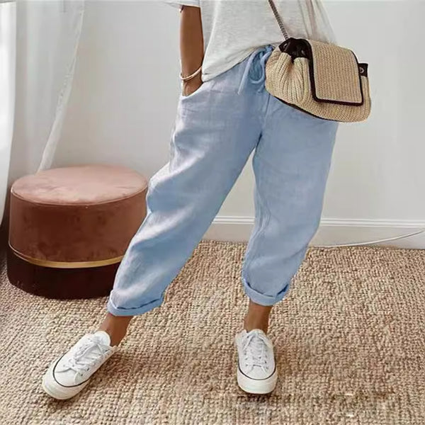 Person wearing light blue jeans and white sneakers with a straw bag, standing on a carpeted floor.