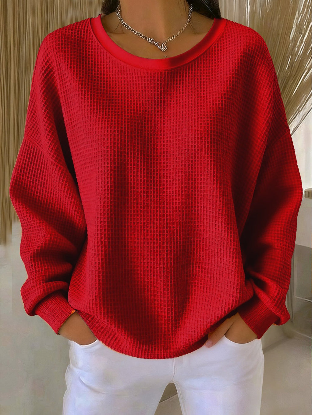 Person wearing a red sweater and white pants against a neutral background