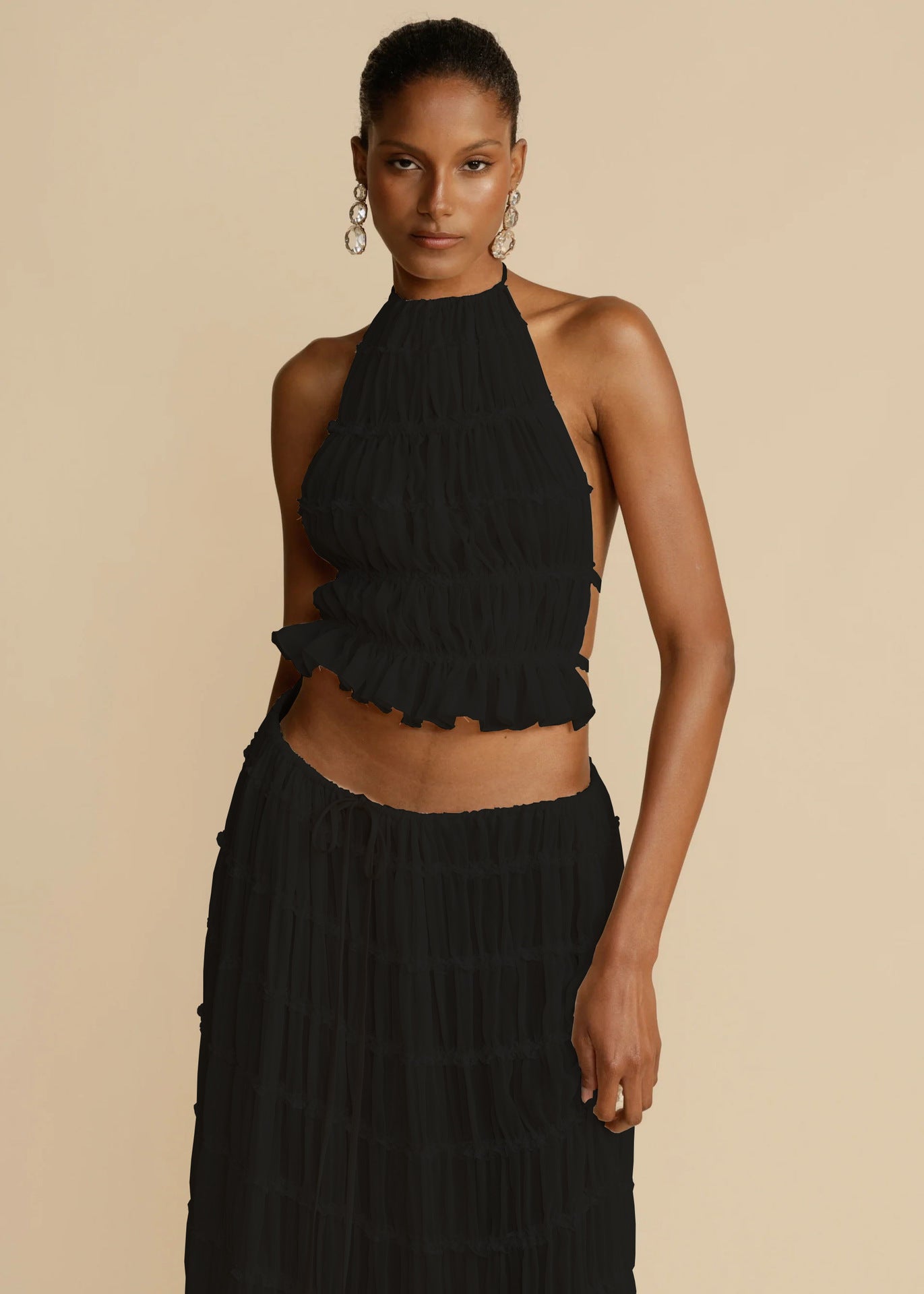 Woman wearing a black halter top and black pants against a beige background