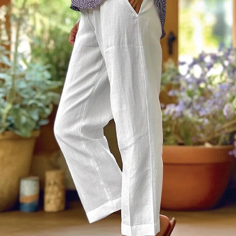 White pants worn by a person standing in a garden with plants and pots in the background.
