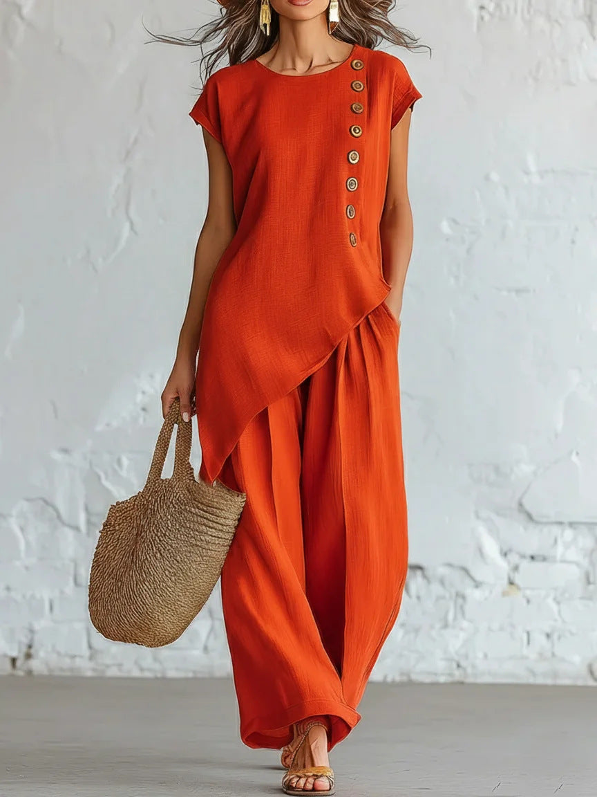 Person wearing an orange dress with button details against a white brick wall.
