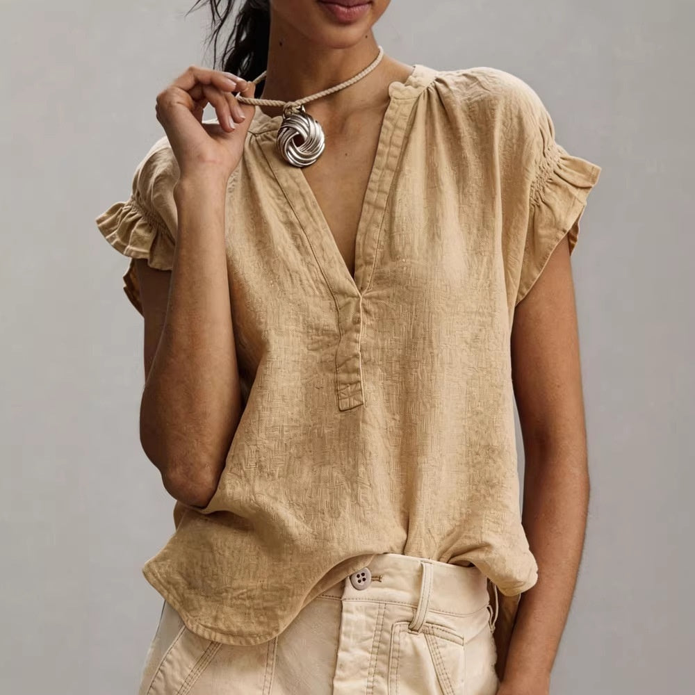 Woman wearing a beige blouse with ruffled sleeves against a gray background