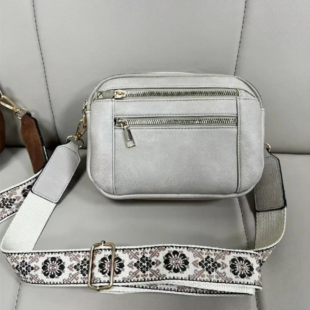 Gray crossbody bag with a patterned strap on a gray surface