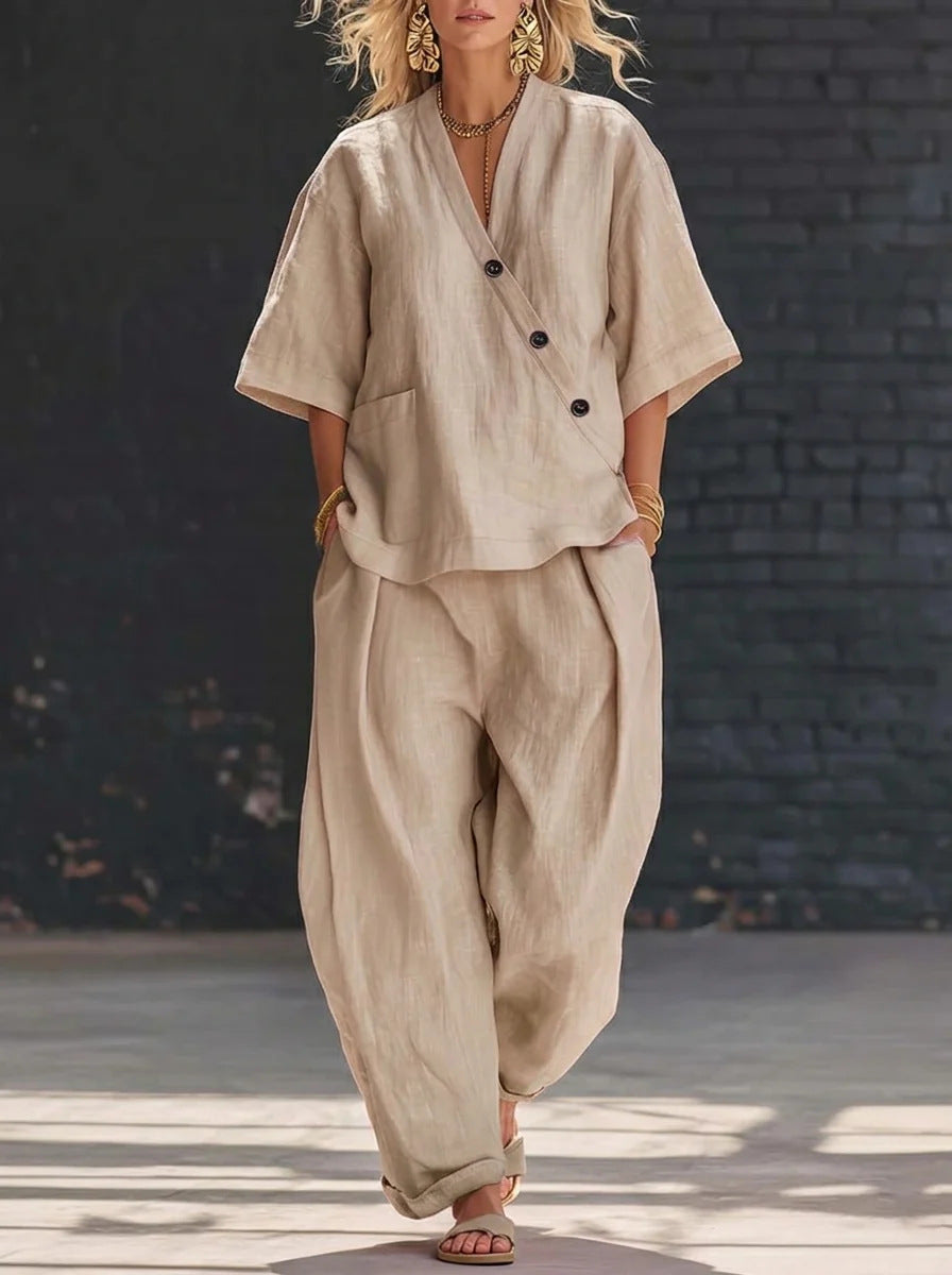 Person wearing a beige linen outfit against a dark brick wall.