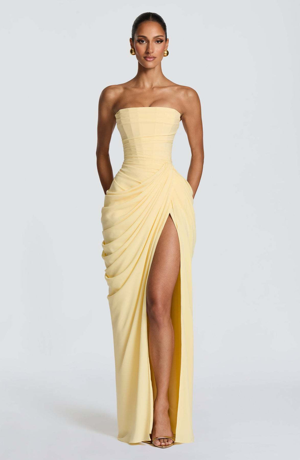 Woman wearing a strapless yellow evening gown with a slit on a white background