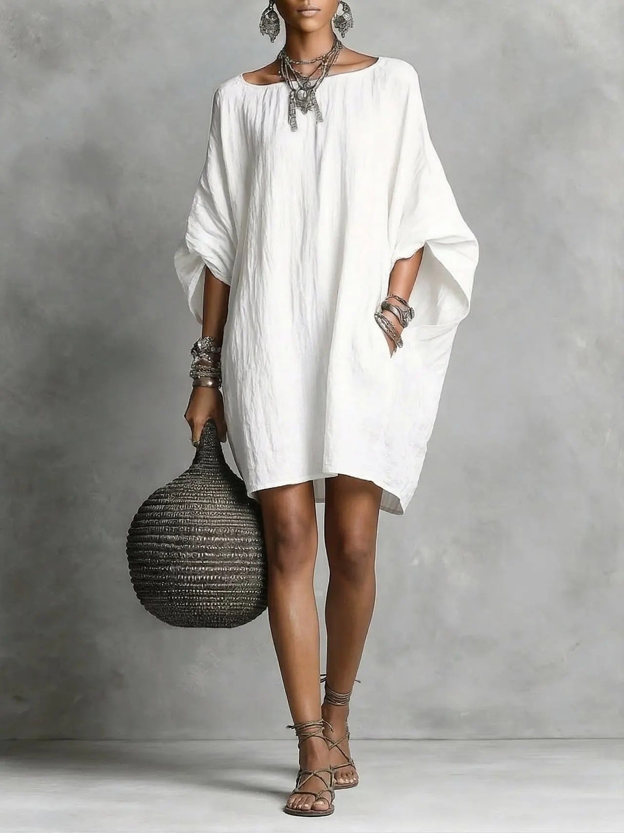 Woman wearing a white dress holding a woven bag against a gray background
