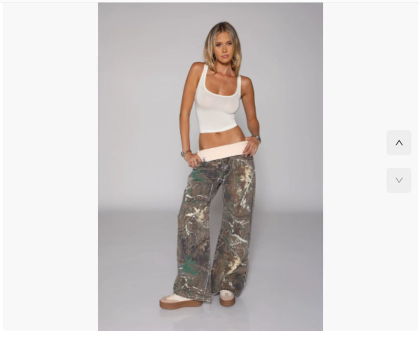 Woman wearing a white tank top and camouflage pants on a gray background