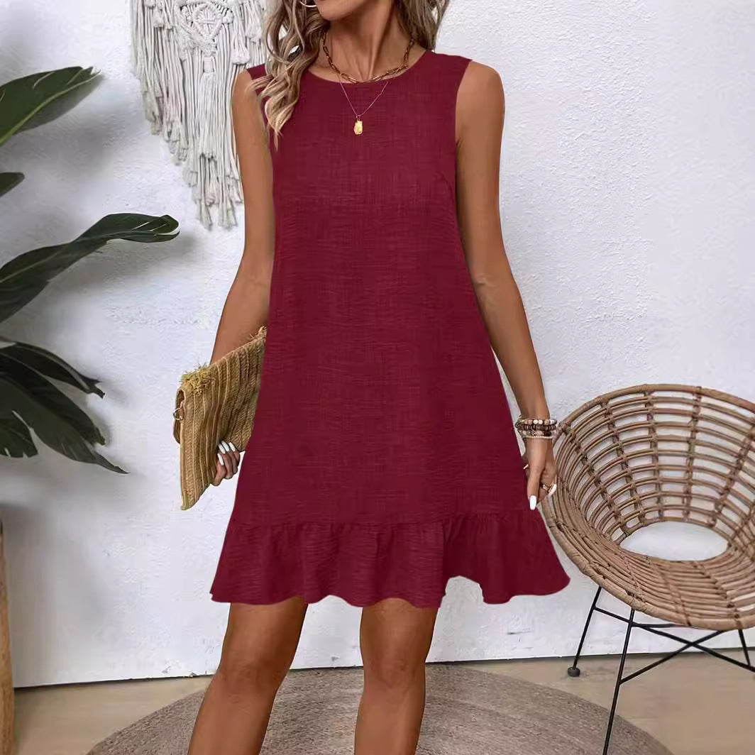 Woman wearing a burgundy dress standing in a room with a plant and wicker chair.
