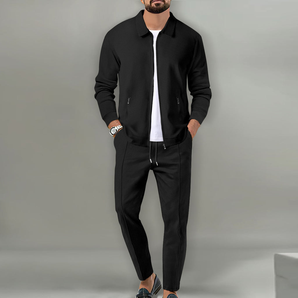 Man wearing a black jacket and pants with a white shirt against a gray background
