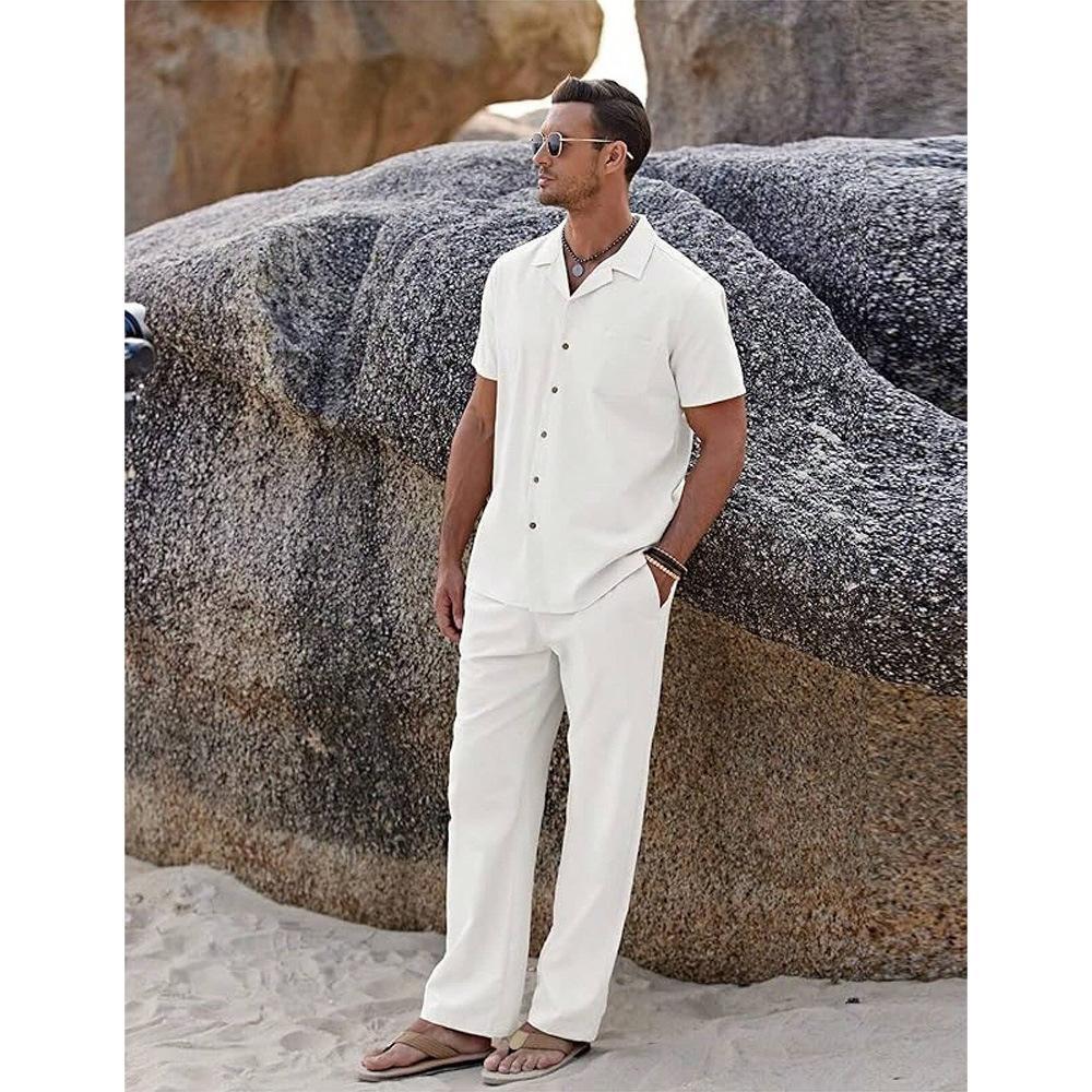 Man in a white outfit standing on a beach with large rocks in the background