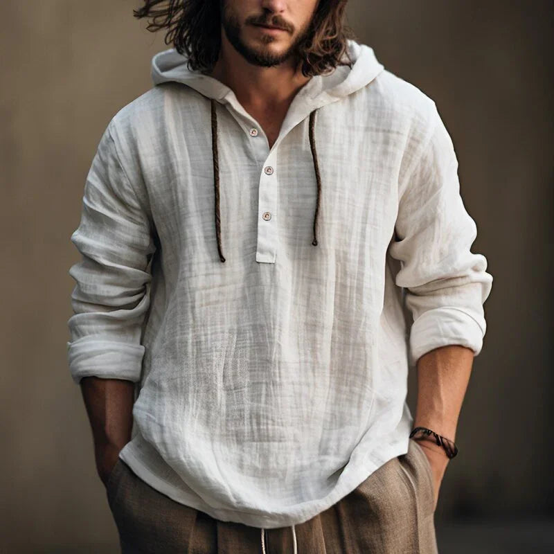 Man wearing a white textured shirt with rolled-up sleeves against a neutral background