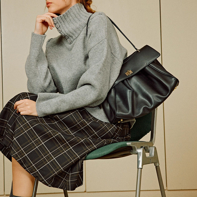 Person wearing a gray sweater and black plaid skirt, sitting on a chair with a black handbag.