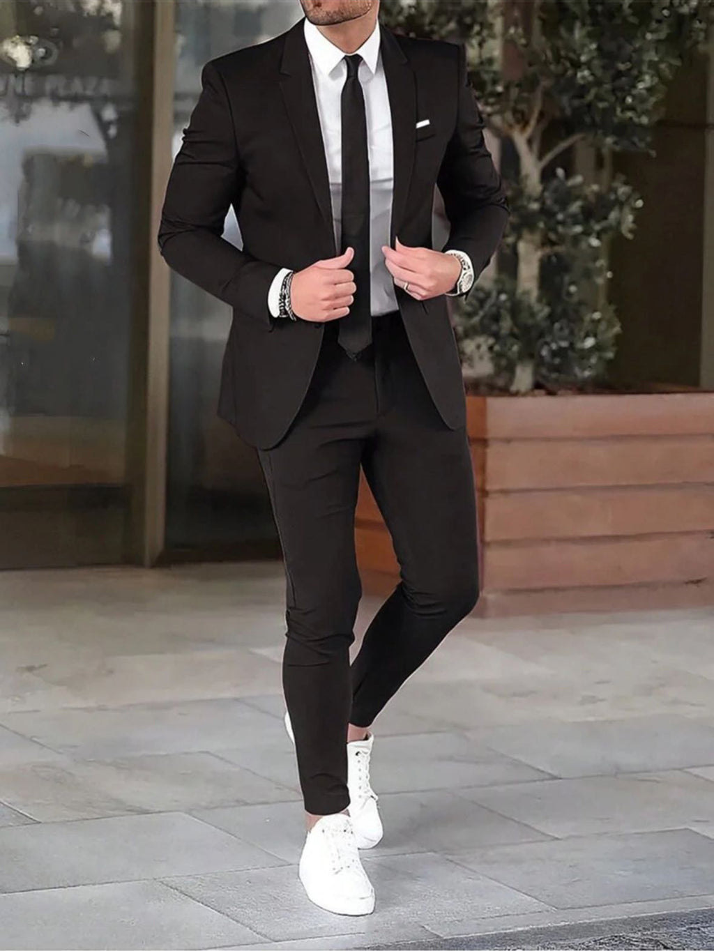 Man wearing a black suit with white sneakers on a city street.