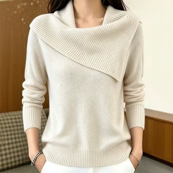 A woman wearing a cream-colored knit sweater with a wide draped cowl neckline and ribbed cuffs and hem, shown from the shoulders to the hips in an indoor setting.