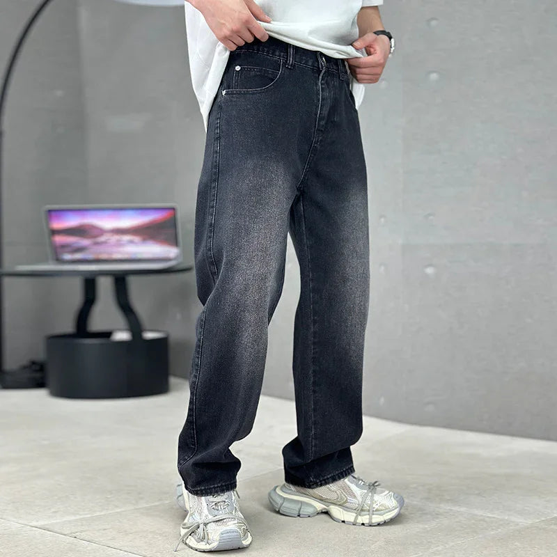 Person wearing black jeans and white sneakers in a room with a gray wall and a computer setup.