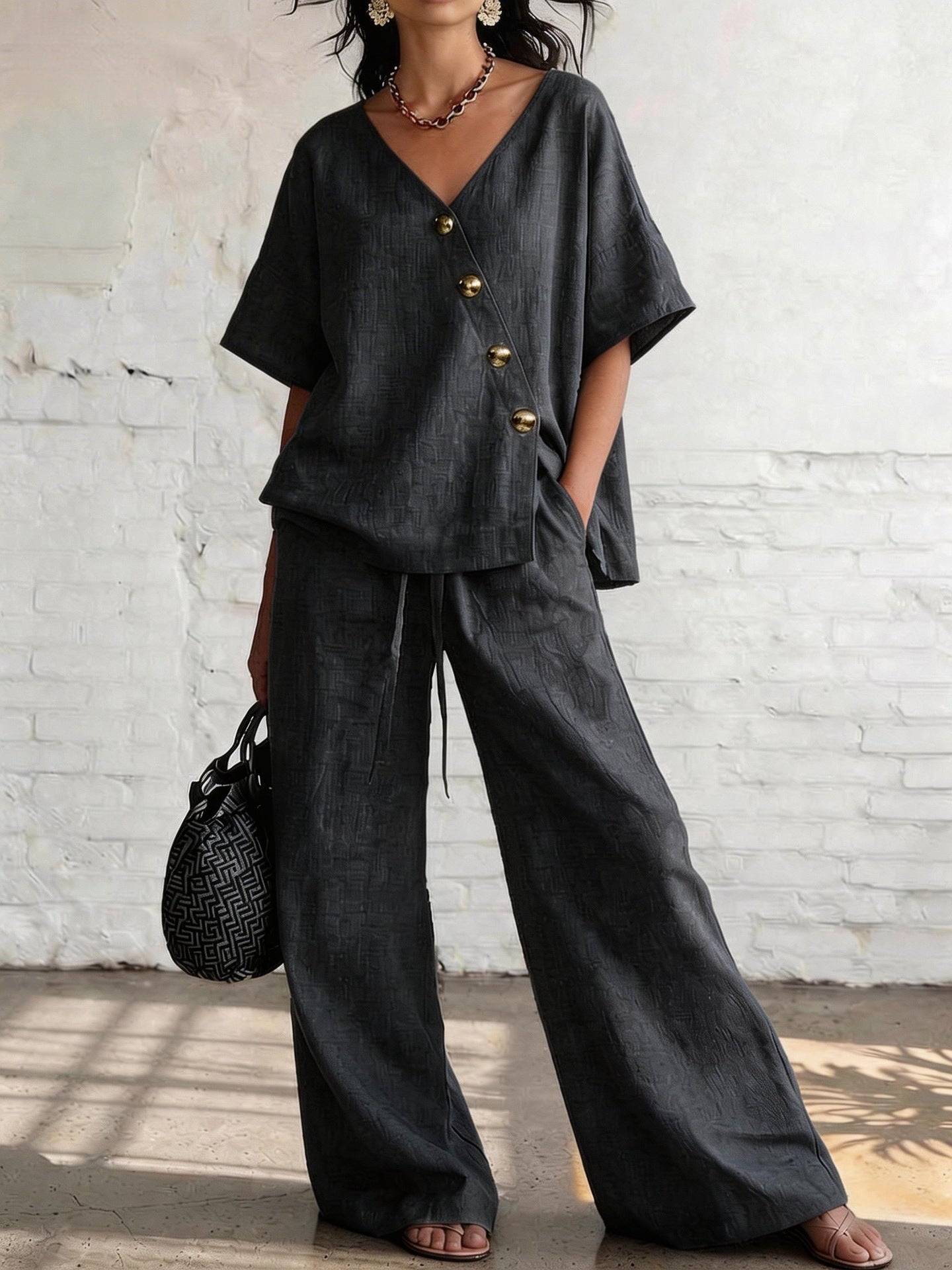 Person wearing a black outfit with wide-leg pants against a white brick wall.