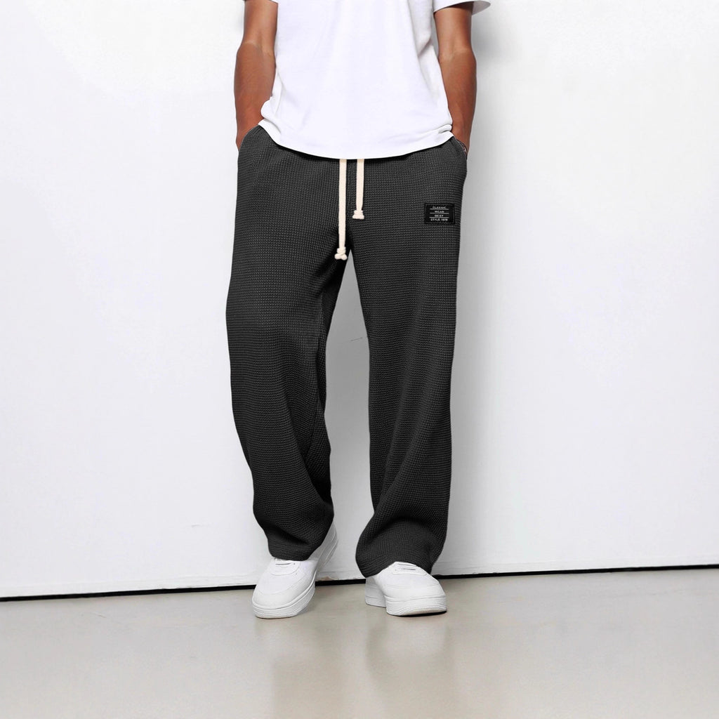 Person wearing black mesh pants with a white drawstring and white sneakers on a plain background