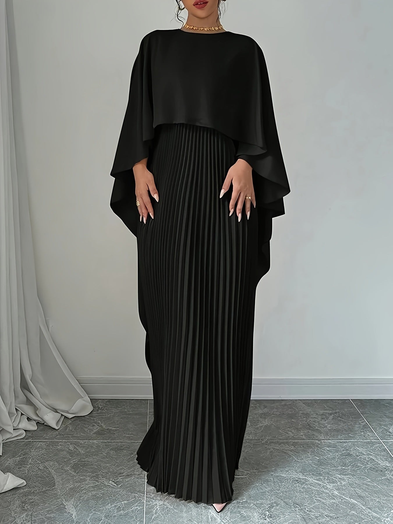 Person wearing a black outfit with a draped top and pleated skirt against a plain background