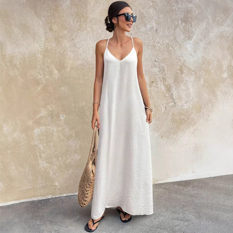 Woman in a white dress holding a straw bag against a textured wall.