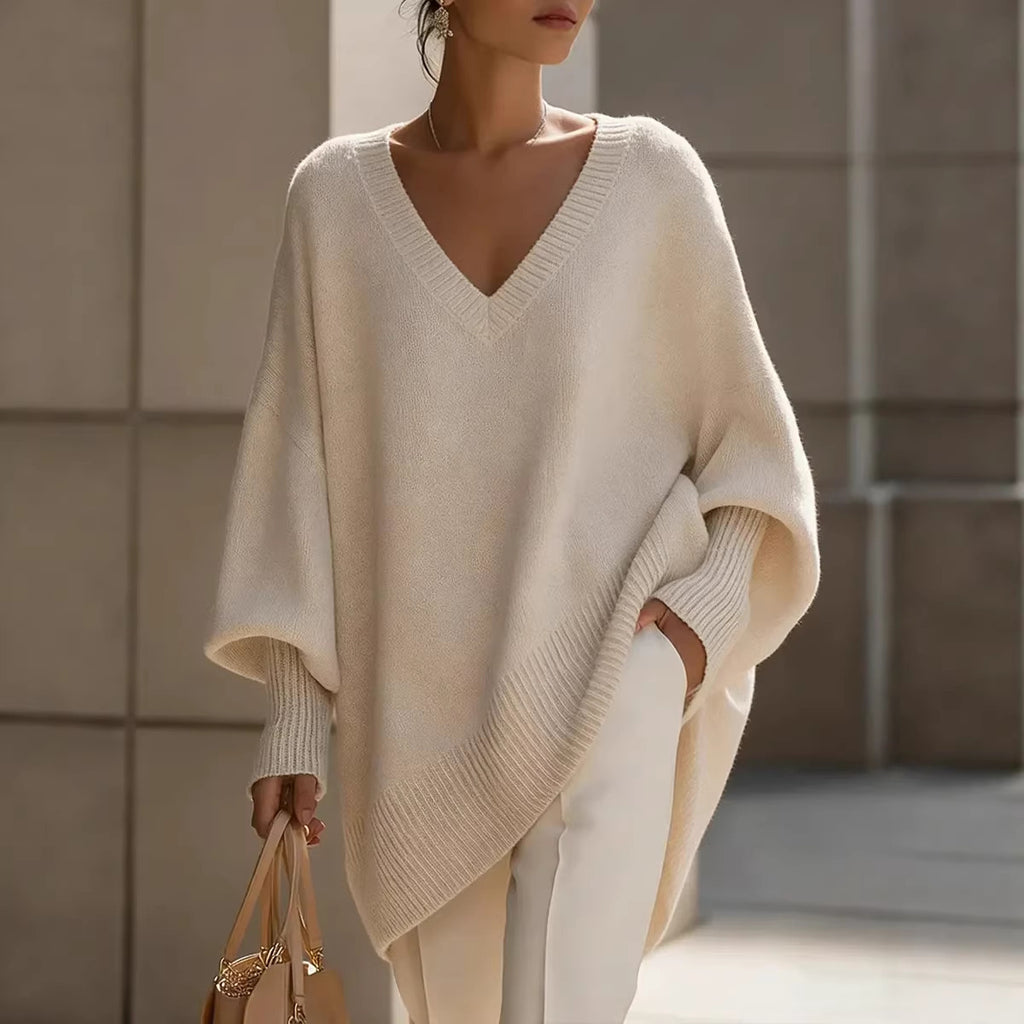 Woman wearing a beige poncho and holding a handbag against a neutral background