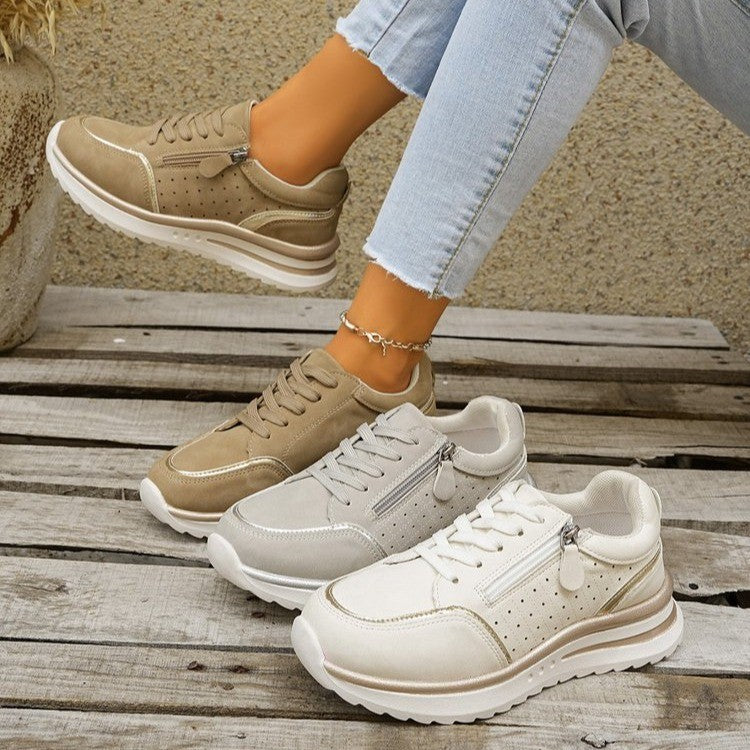 Two pairs of sneakers, one beige and one white, on a wooden surface.