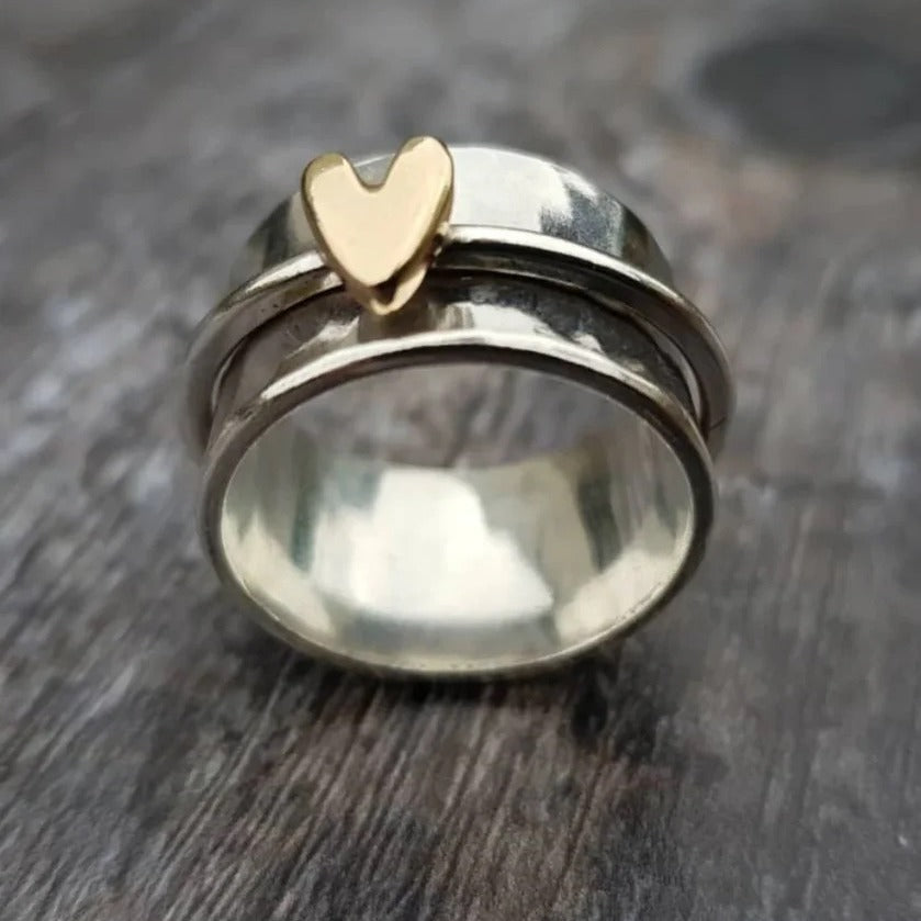 Silver ring with a gold heart-shaped accent on a wooden surface
