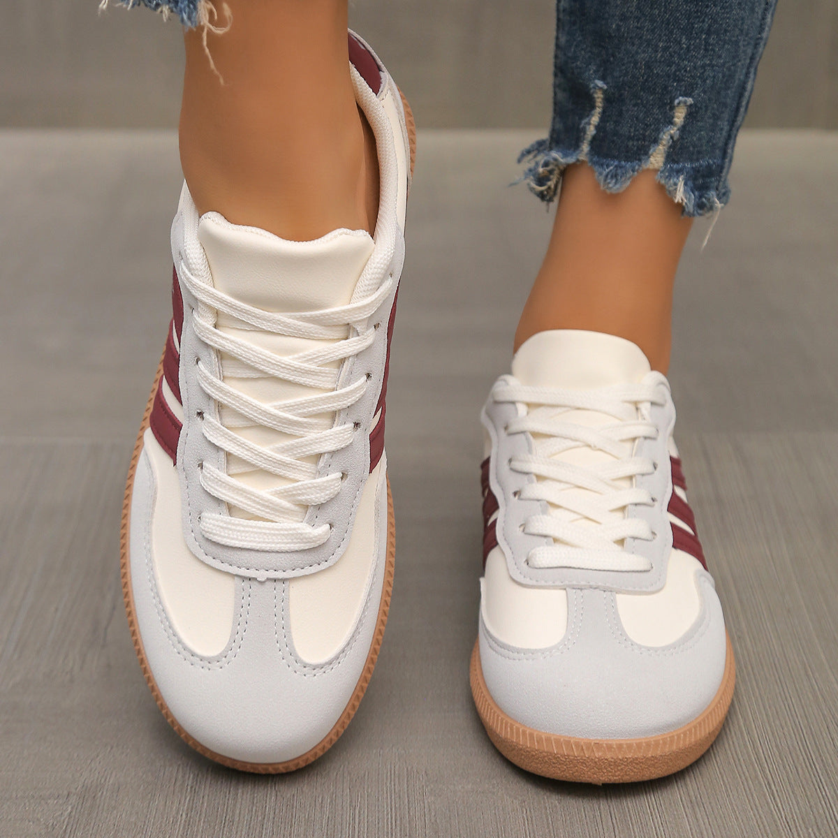 White and red sneakers with brown soles worn by a person on a wooden floor.