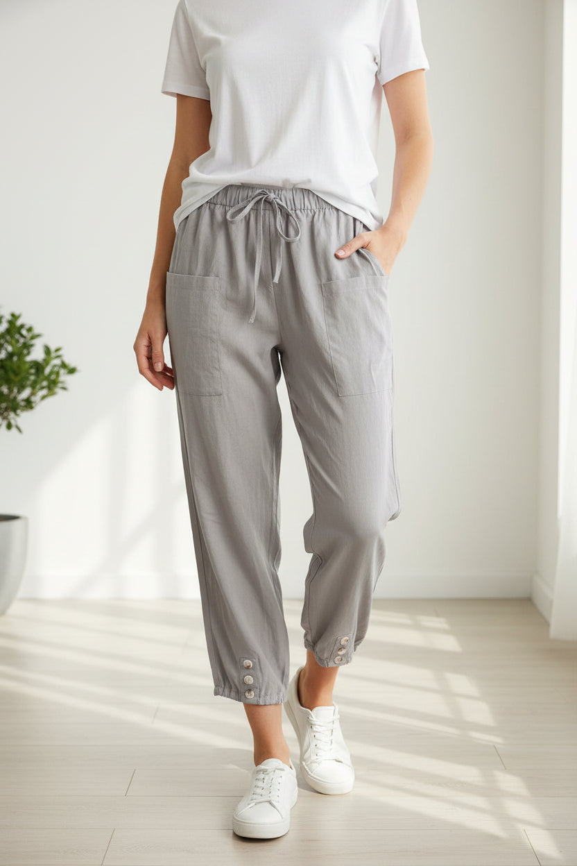 Gray pants with drawstring waist and button details worn by models on a light wooden floor.